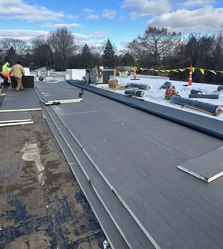 New insulation board and membrane being laid over a commercial roof tear-off during a Northern Indiana winter