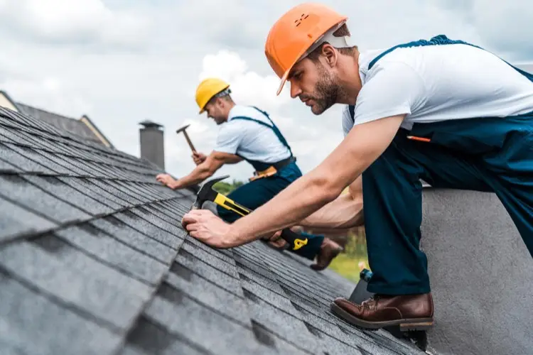 Close up of two roofers installing new shingles on a pitched roof