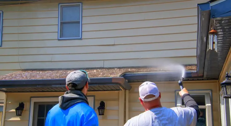Two men standing on ground using garden hose to clean lower roof