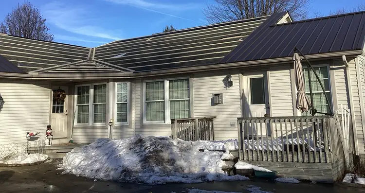 Furring boards screwed across old asphalt shingles on a Goshen Indiana home, with new burnished slate exposed fastener metal panels already on the right-hand section