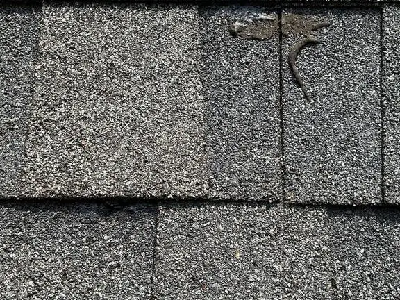 Close-up of a weathered asphalt shingle roof showing granule loss and a cracked shingle sealed with roof cement