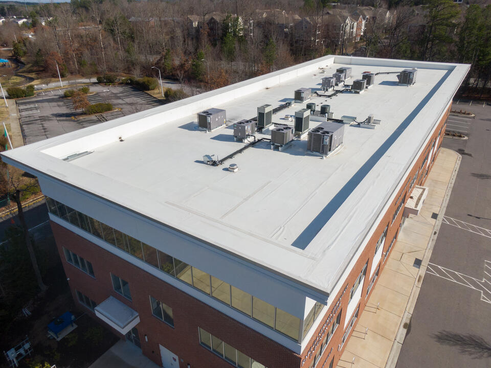 brick commercial building with brand new white commercial roofing with hvac appliances near the center of the roof