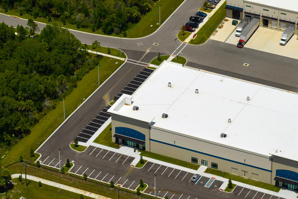 drone view of new white commercial roofing on a building surrounded by a parking lot