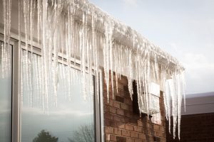 how to prevent ice dams on roof-brick house with ice and snow built up on roof and icicles hanging off roof edge