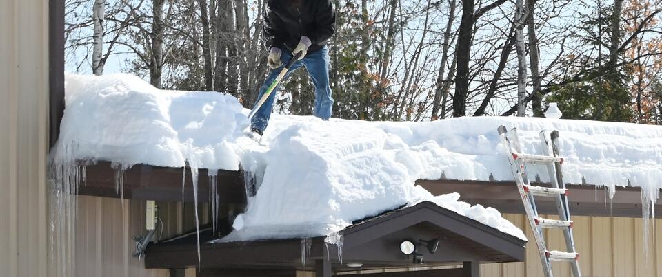 how to prevent ice dams on roof-man removing loads of snow off his roof